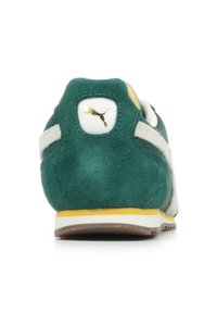 Sneaker verde in suede con una striscia bianca, accenti gialli e logo Puma dorato sul tallone. Presenta una parte posteriore testurizzata e una suola in gomma.