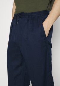 Mörkblå, lätta byxor med elastisk midja och dragsko. Har sidofickor och en avslappnad passform. Mjuk, texturerad tyg.