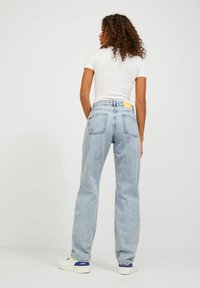 Šviesiai mėlynos, aukštu liemeniu, laisvo kirpimo džinsai su klasikinėmis užpakalinėmis kišenėmis ir geltonu ženkliuku ant liemens. Dėvima su balta palaidine.