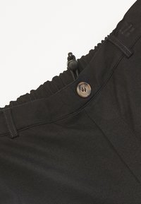 Pantalon noir avec une ceinture élastique dotée d'un cordon de serrage et d'une fermeture à bouton unique. Le tissu est lisse avec des détails de couture minimaux.