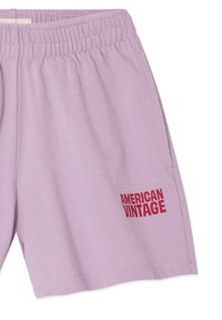 Shorts en coton lilas avec une taille élastique, arborant un logo rouge "AMERICAN VINTAGE" en bas à gauche. Texture lisse, coupe décontractée.