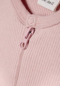 Lichtroze geribbelde stof romper met een roze rits en drukknoopsluiting bij de hals. Label zichtbaar met maatdetails.