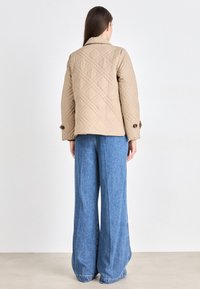 Beige quilted jacket with a collared neckline and buttoned cuffs, paired with wide-leg blue denim jeans.