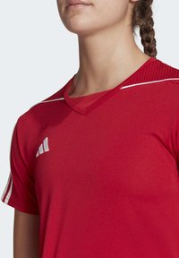 Maglietta sportiva rossa con scollo a V e maniche corte, caratterizzata da dettagli bianchi e un design texturizzato sulle spalle. Realizzata in tessuto leggero.