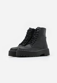 Black leather ankle boots with a chunky platform sole, featuring lace-up closure, side zipper, and white stitching accents.