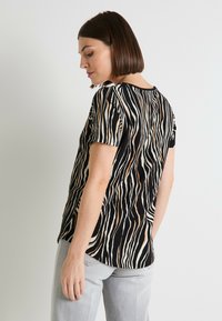 Camiseta de manga corta negra con un patrón de rayas onduladas en crema y marrón, con un corte relajado y un cuello redondo.