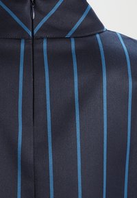 Tessuto blu navy con strisce verticali azzurro chiaro, caratterizzato da un colletto alto e una chiusura con zip sul retro. Texture liscia con un aspetto lucido.