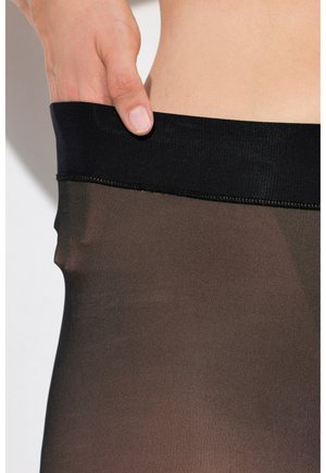 Zwarte tailleband van doorschijnende, gestructureerde panty in een donkere tint, vastgehouden door een hand, met fijne stiksels zichtbaar langs de randen.