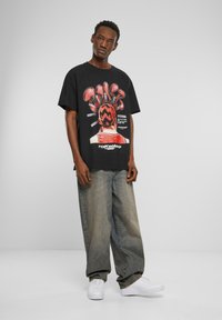 Svart grafisk t-skjorte med en fargerik illustrasjon på baksiden, kombinert med løse lys-blå denimjeans og hvite sneakers.