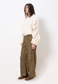 Veste crème surdimensionnée avec des manches froncées, associée à un pantalon large imprimé léopard. Des sandales brunes à lanières complètent la tenue.