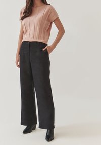 Světle růžový pletený top se skládaným výstřihem spárovaný s černými širokými kalhotami s vysokým pasem a černými kotníkovými botami.