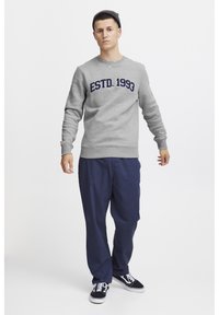 Grå hettegenser med "ESTD. 1993" i marineblå, kombinert med marineblå bukser og svarte sneakers, med en avslappet passform og ribbestrikkede mansjetter.