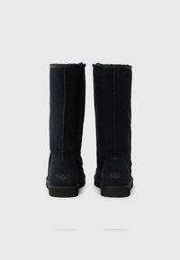 Svarta knähöga stövlar i mocka med en slät yta, sydda sömmar och gummisulor; har en logotyp på hälen.