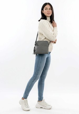 Gray crossbody bag with textured material, zip closure, and tassel detail, paired with a cream cable-knit sweater and light blue jeans.