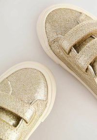 Baskets dorées à paillettes avec des sangles Velcro, semelles en caoutchouc crème, bout arrondi et dessus texturé pour une esthétique rehaussée.
