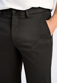 Pantaloni neri con una trama liscia, taglio dritto, tasche laterali e una cintura con chiusura a bottone.