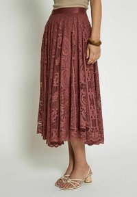 Gonna in pizzo color rosa con pieghe, caratterizzata da un intricato motivo paisley. Lunghezza sotto il ginocchio, orlo rifinito con dettagli a scallop.
