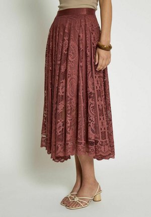 Jupe en dentelle rose avec des plis, arborant un motif paisley complexe. Longueur sous le genou, ourlet festonné.