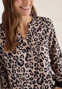 Bluzka w panterkę z miękkiego materiału o jasnobeżowym tle i czarnych plamkach, z płytkim dekoltem w serek i długimi rękawami.