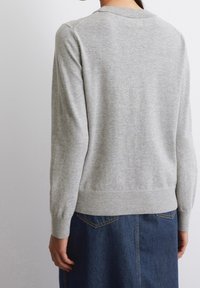 Jasnoszary sweter z długimi rękawami, żebrowanymi mankietami i dołem. Miękka dzianina, prosty design, widok z tyłu. Połączony z dżinsową spódnicą.