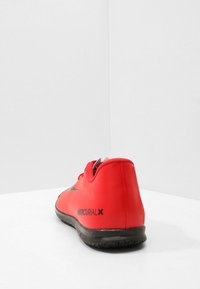 Zapatos de fútbol sintéticos rojos con un diseño elegante, acentos negros y un área posterior acolchada. Presentan una suela texturada para mayor tracción.