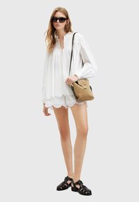 Blusa bianca con dettagli arricciati e orlo scallop, abbinata a una borsa a tracolla beige con hardware dorato e sandali neri con cinghie.