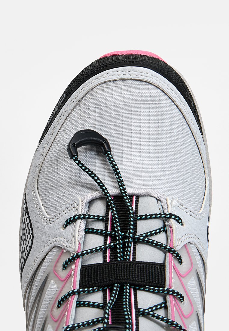 Scarpa sportiva grigia con tomaia testurizzata, accenti neri e dettagli rosa. Presenta lacci elastici e una chiusura a toggle sicura.