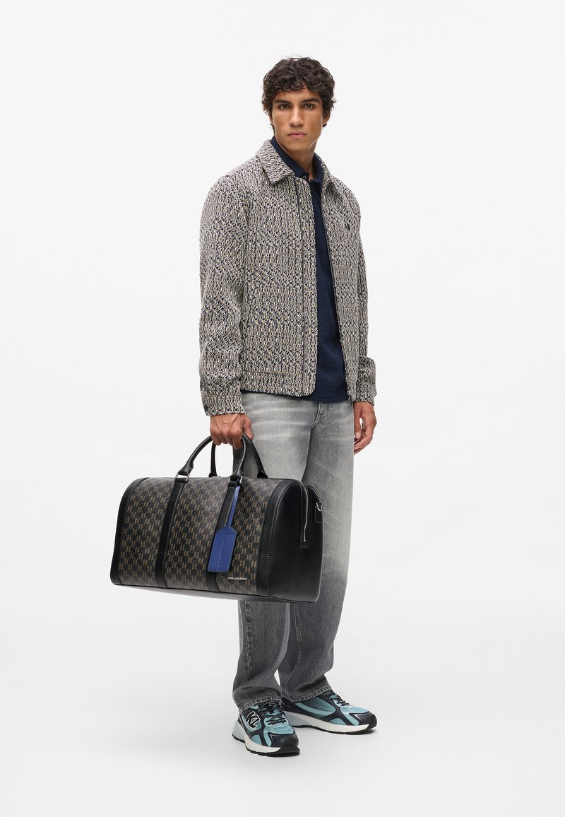 Izšūts tekstila žakets, tumši zils krekls, gaiši pelēki džinsi, nēsā melnu un brūnu rakstainu somu ar zilu birku; sporta apavi ar melniem un tumši ziliem akcentiem.