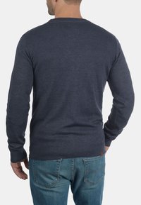 Mörkblå tröja i ribbad stickning med långa ärmar och axelklaffar, i kombination med ljusblå jeans.