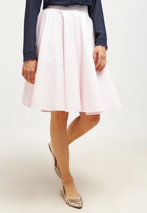 Jupe trapèze rose clair en tissu lisse, avec un ourlet à hauteur du genou. Associée à un chemisier bleu marine et des ballerines beiges à pois.