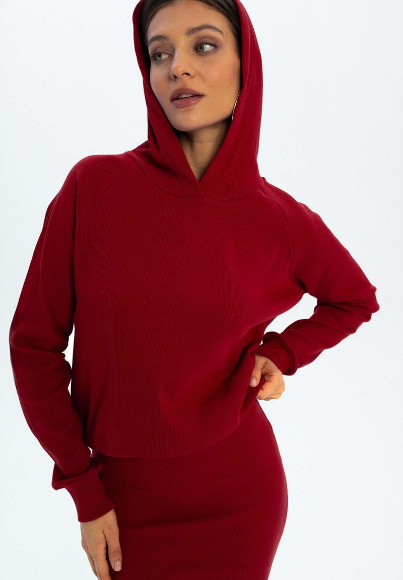 Czerwona, żebrowana bluza z kapturem o dopasowanym kroju, z długimi rękawami, zestawiona z dopasowaną spódnicą. Gładka tekstura.