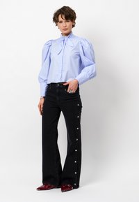 Blue puff-sleeve blouse with neck tie, paired with high-waisted black jeans featuring snap accents along the sides. Red pointed toe shoes.
