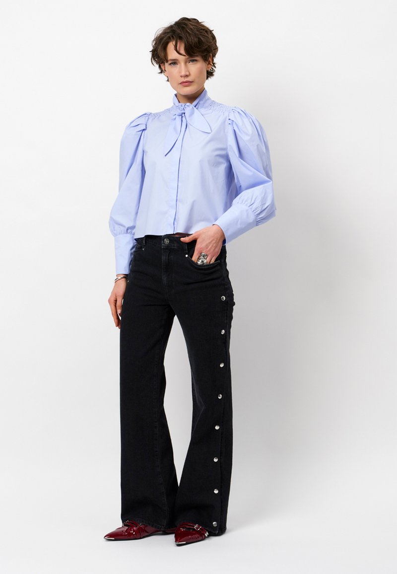 Blue puff-sleeve blouse with neck tie, paired with high-waisted black jeans featuring snap accents along the sides. Red pointed toe shoes.
