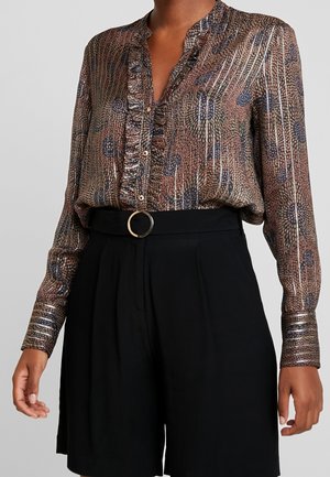 Blusa marrone con motivo, caratterizzata da un fronte arricciato, maniche lunghe con polsini abbottonati e scollature a V. Abbinata a pantaloni corti neri a vita alta.
