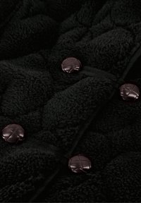 Zwart fleece-stof heeft een gequilt oppervlak met grote, donkerbruine knoopsluitingen en zichtbare stiksels.