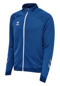 Niebieska sportowa kurtka z pełnym zamkiem błyskawicznym, białym suwakiem, logo hummel na klatce piersiowej oraz odblaskowymi wzorami w kształcie jodełki na rękawach i ramionach.