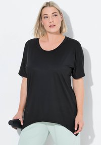 Černý top s krátkým rukávem a kulatým výstřihem. Měkká látka s volným střihem, který má boční rozparek. Model drží černou láhev na vodu.