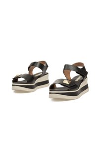 Sandalias negras de plataforma con diseño de tiras cruzadas, superficie texturizada, tachuelas en dorado y suela de goma blanca con una franja negra.