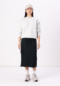 Grijze sweatshirt, zwarte midi rok met cargozakken, lichtbeige pet en lichte sneakers met witte sokken. Eenvoudige, functionele kleding.