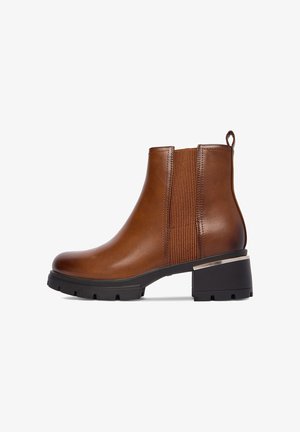 Pruunast nahast pahkluu pikkune saabas, millel on elastsed küljetükid, ümar ninamik ja must jämeda kontsaga, mille kontsil on metallikaktsent.