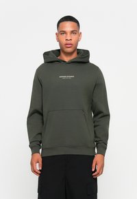 Grøn hættebluse med kængurulomme, der har teksten "WEEKEND OFFENDER ADMIT NOTHING" i hvid foran. Fremstillet af blødt, tykkere stof.