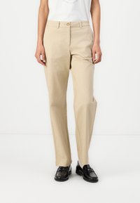 Beige pamut nadrág, egyenes szabású, elöl gombos zárással és övhurkokkal, fekete mokaszinnal párosítva.