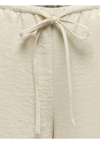 Gros plan sur un short en tissu beige avec une taille à cordon nouée, montrant la texture et les détails des coutures.