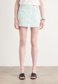 Mätovo zelená denim mini sukňa s predným zipsom, dvoma bočnými vreckami a rovnými strihom. V kombinácii s čiernymi otvorenými sandálmi.