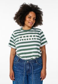 T-shirt rayé vert et blanc avec "CASUAL ELEGANCE" imprimé en beige, associé à un jean en denim bleu taille haute. Tissu doux, coupe décontractée.