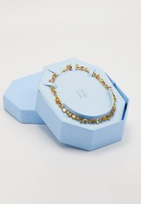 Gold necklace with yellow and amber gemstones displayed in a light blue octagonal jewelry box with lid beside it.
