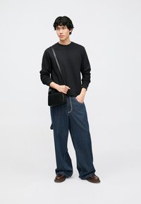 Fekete hosszú ujjú pulóver, széles kék csíkos nadrág, barna cipők és egy kis fekete keresztpántos táska. Hétköznapi öltözék neutrális háttér előtt.