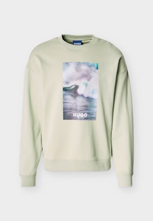 Svetlo bež pulover z velikim pravokotnim motivom oceanskega vala in napisom "HUGO" na sredini sprednjega dela, z rebrastimi manšetami in spodnjim robom.