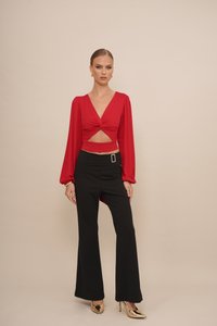 Red long-sleeve top with a twisted front and cutout, paired with black high-waisted flared pants. Gold-accented heels complete the look.