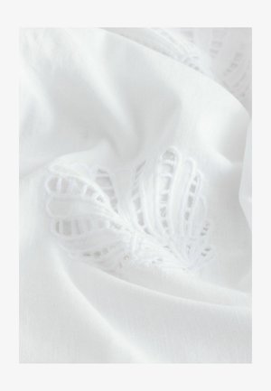 Witte stof met textuurrijke, geborduurde bladerenpatronen. Het ontwerp bevat delicate uitsparingen die de zachte, gladde textuur benadrukken.